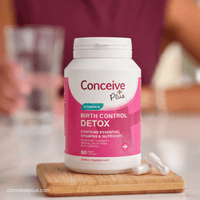 Conceive Plus birth control detox supplement bottle on a wooden cutting board with blurred background