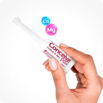 Conceive Plus Fertility Lubricant (8x4g Pre-filled Applicators) shown being held between two fingers with a firm grip, highlighting slim, ergonomic design of applicator; blue and pink icons for calcium (Ca) and magnesium (Mg) ions float nearby to emphasize product’s patented formulation.